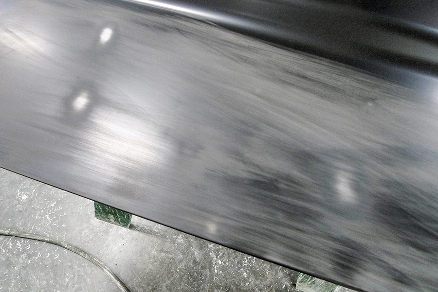 Close-up of a black automotive body panel showing fine white dust patterns after a professional hand-sanding process.