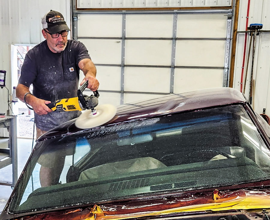 Professional auto body technician using a DeWalt rotary polisher to buff the roof of a classic maroon Chevrolet Chevelle SS for a high-gloss finish.