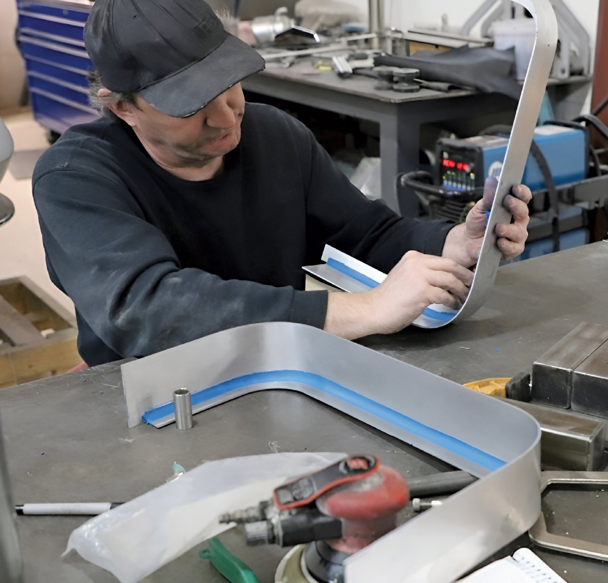 Fabricator shaping a custom aluminum trim piece on a metal workshop table.