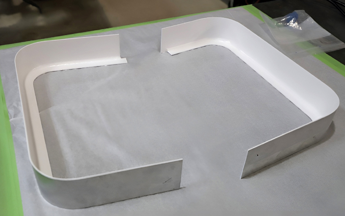 Two custom-shaped white metal trim components resting on a work surface.