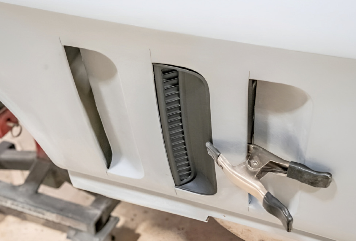 A black vent being clamped into place on a white car fender during assembly.