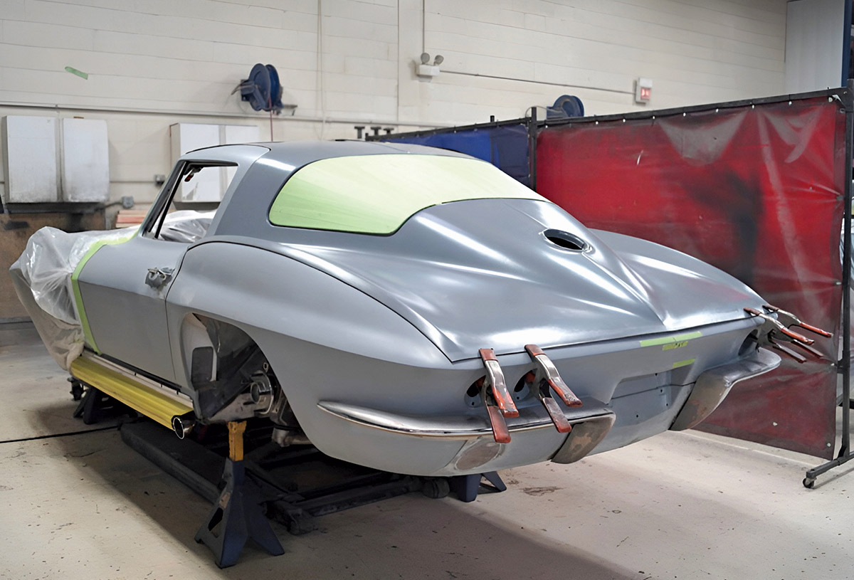 Rear view of a grey 1965 Corvette body on stands with clamps on the rear panel.
