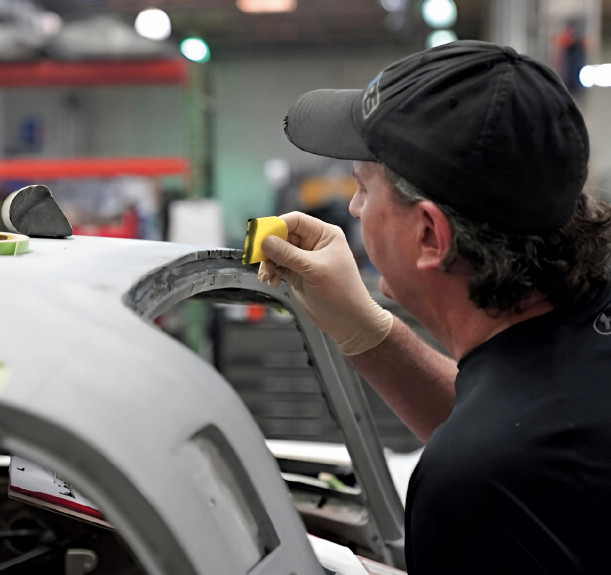 Mechanic using a yellow tool to sand the window frame of a car.