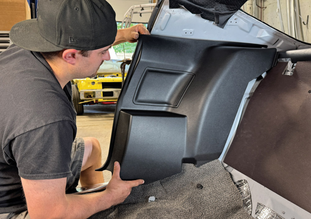 Pat O’Brien aligns a molded black plastic rear interior side panel against the inner body of the white Camaro, just above the grey looped carpet.