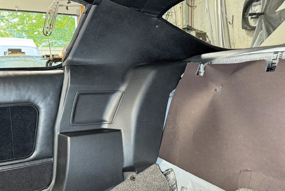 Interior view of the Camaro’s rear passenger area with black lower side and upper sail panels installed. The rear seat area is empty, revealing insulation on the bulkhead.