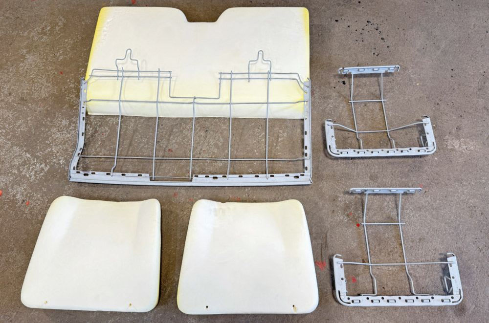 Three freshly painted grey metal wire seat frames and a matching set of three white molded foam cushions are laid out on a concrete floor.