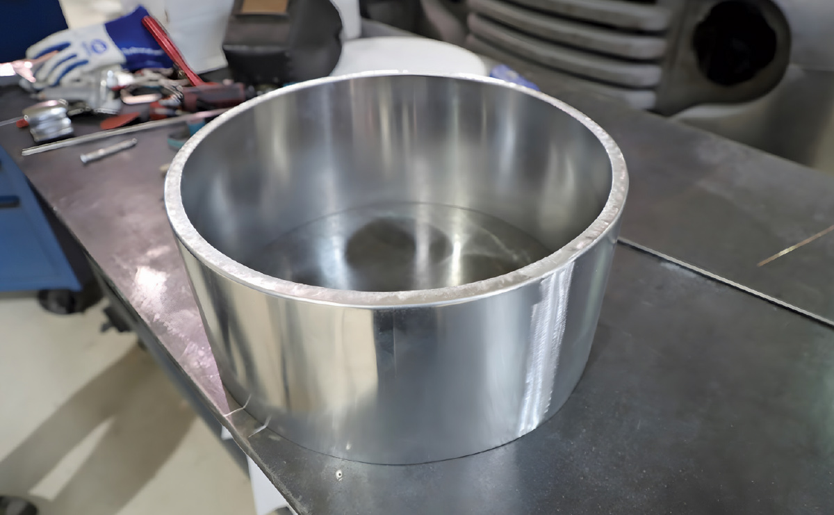 A completed circular aluminum ring component sitting on a dark metal workbench.