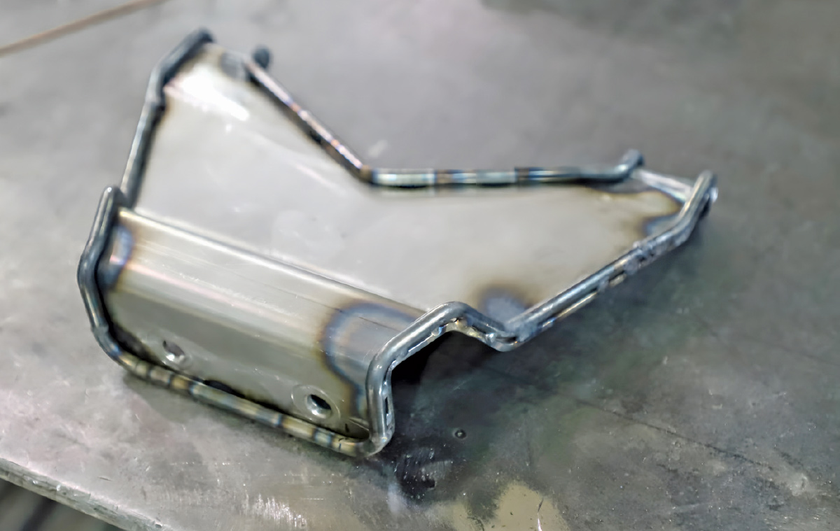 A small, custom-welded aluminum mounting bracket on a metal workbench.