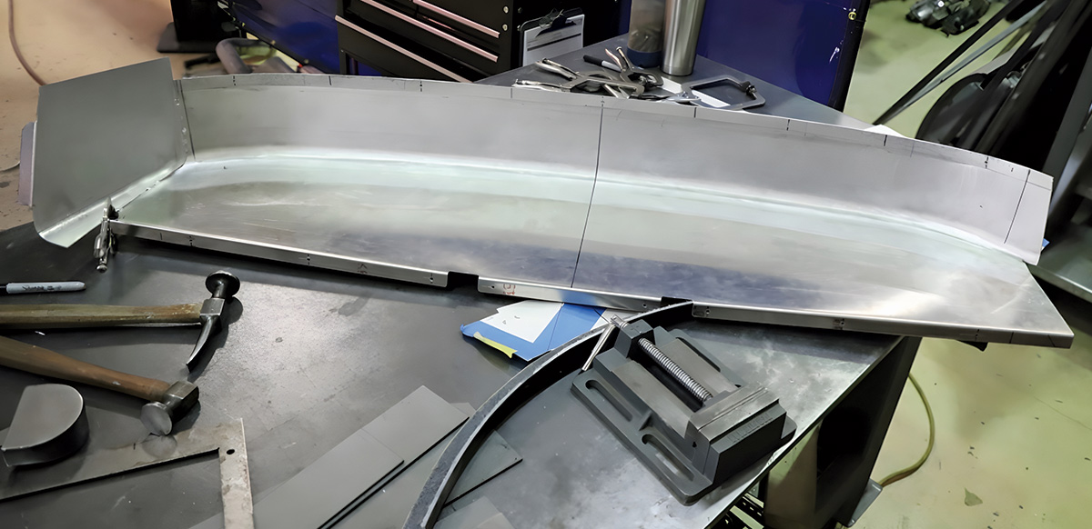 Long piece of sheet aluminum being prepared on a workbench for fabrication.