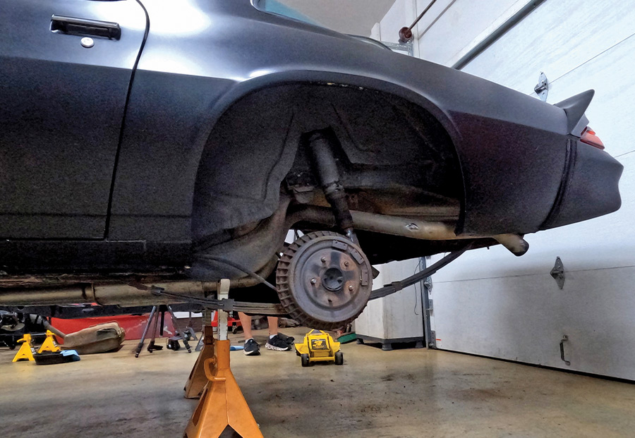 Side profile of a black 1970s Chevrolet Camaro project car on jack stands, showing the rear wheel well, leaf spring suspension, and original drum brakes during a restoration