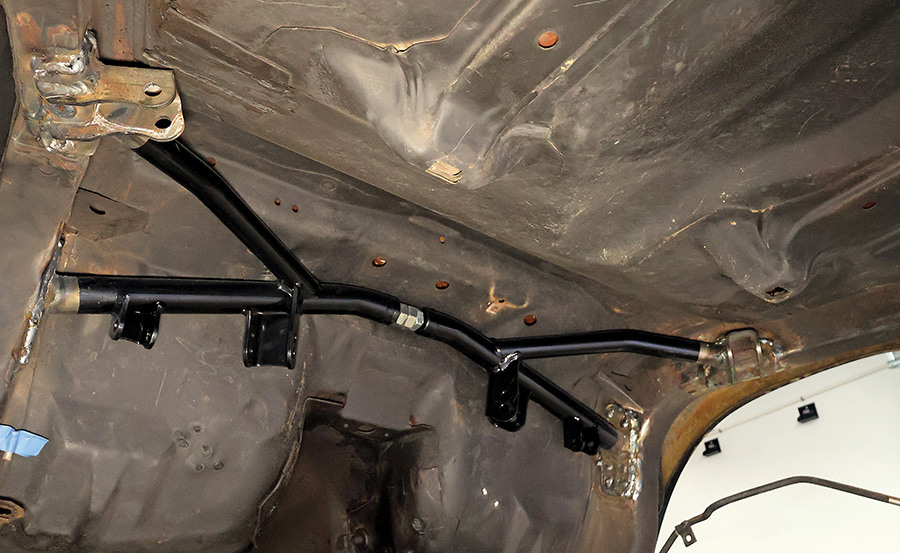 A newly installed black powder-coated rear suspension torque arm and crossmember reinforcement professionally welded into the chassis of a classic car project