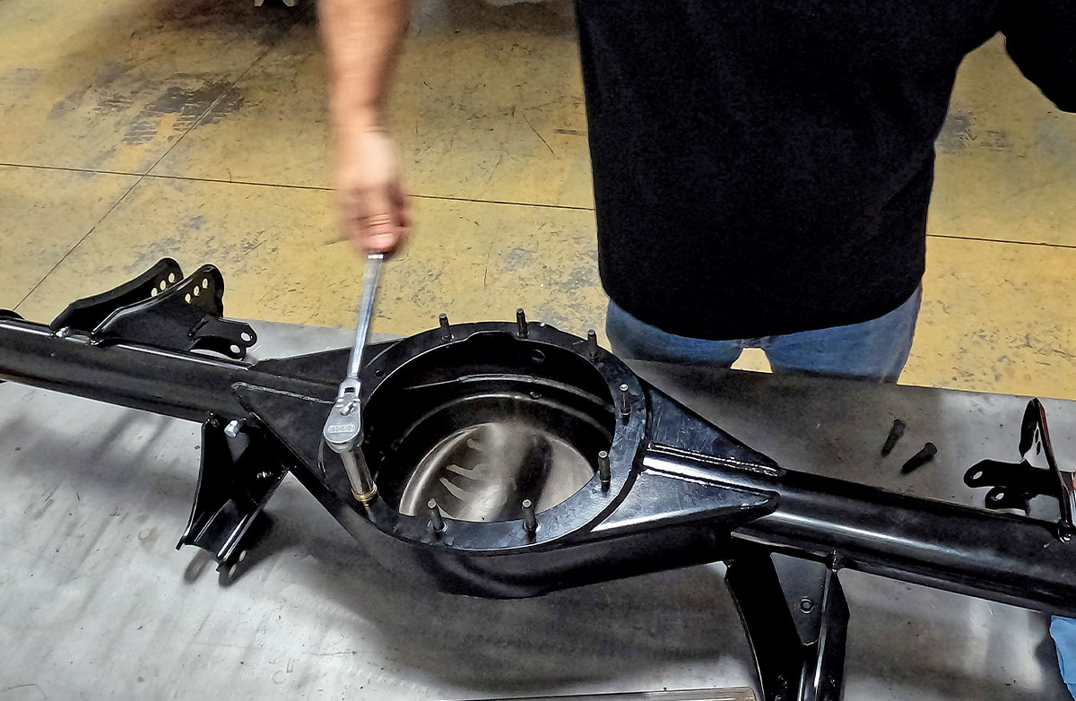 A mechanic using a socket wrench to tighten mounting bolts on a black powder-coated Ford 9-inch rear differential housing during a high-performance classic car restoration