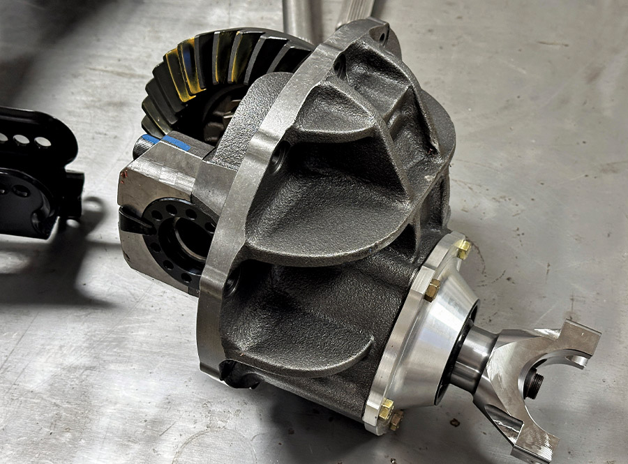 A detailed view of a differential center section assembly showcasing the ring gear with yellow marking compound, a reinforced casting, and a silver aluminum pinion support on a metal workbench