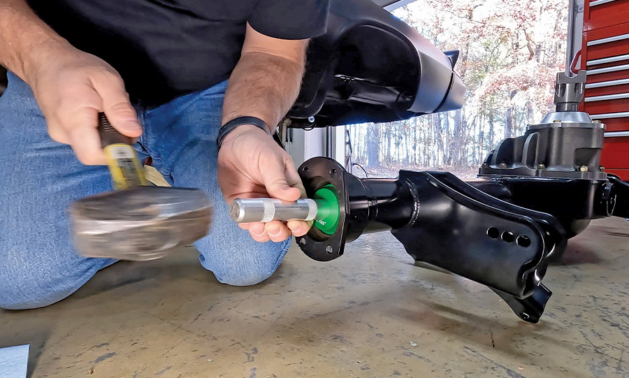 A mechanic using a dead-blow hammer and a seal driver tool to install rear axle seals into a new black powder-coated Ford 9-inch housing for a classic car project