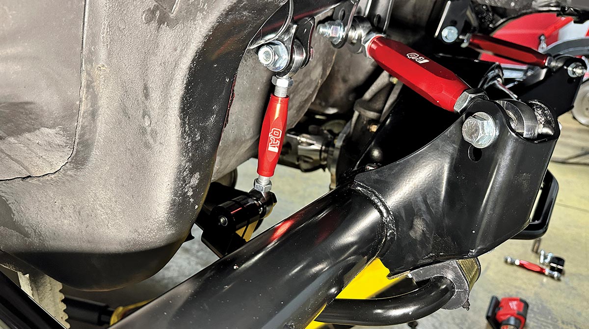 A detailed undercarriage view of the final installation of a QA1 rear suspension system on a classic car, featuring adjustable red panhard rods and a black powder-coated axle housing