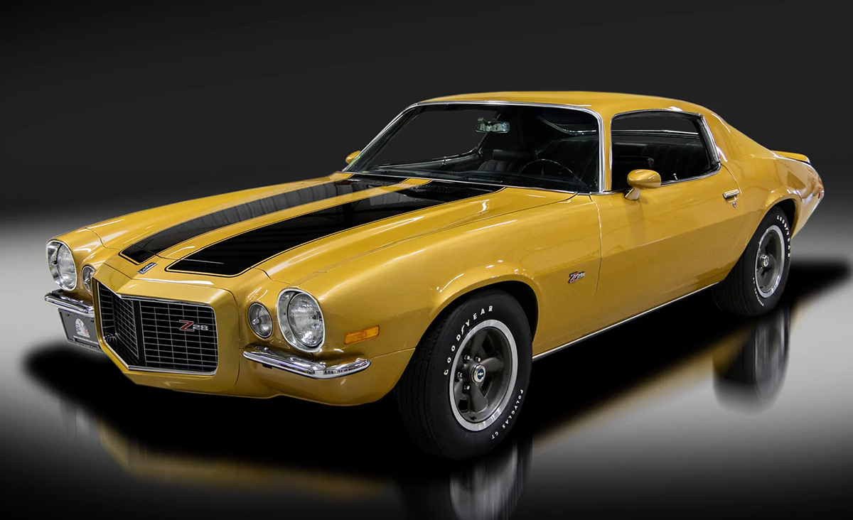 A polished classic yellow Chevrolet Camaro Z28 with black racing stripes on a reflective dark surface.