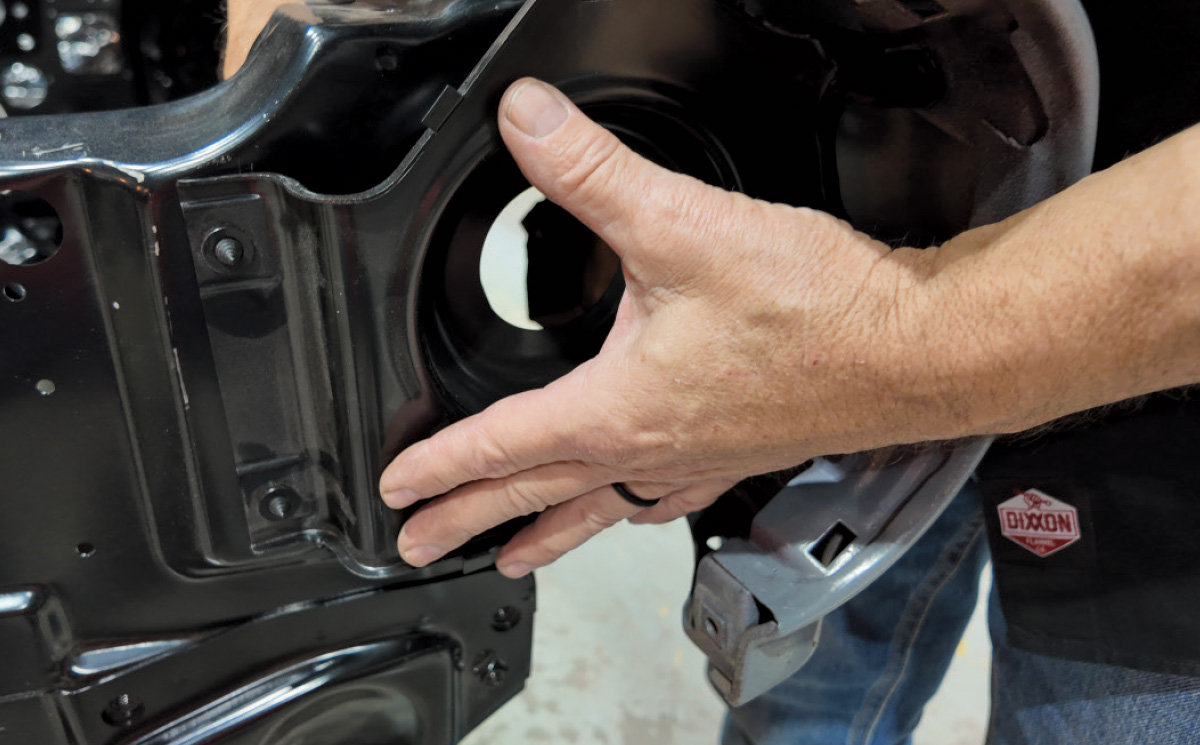 A hand aligns a black metal part against a blue car fender piece.