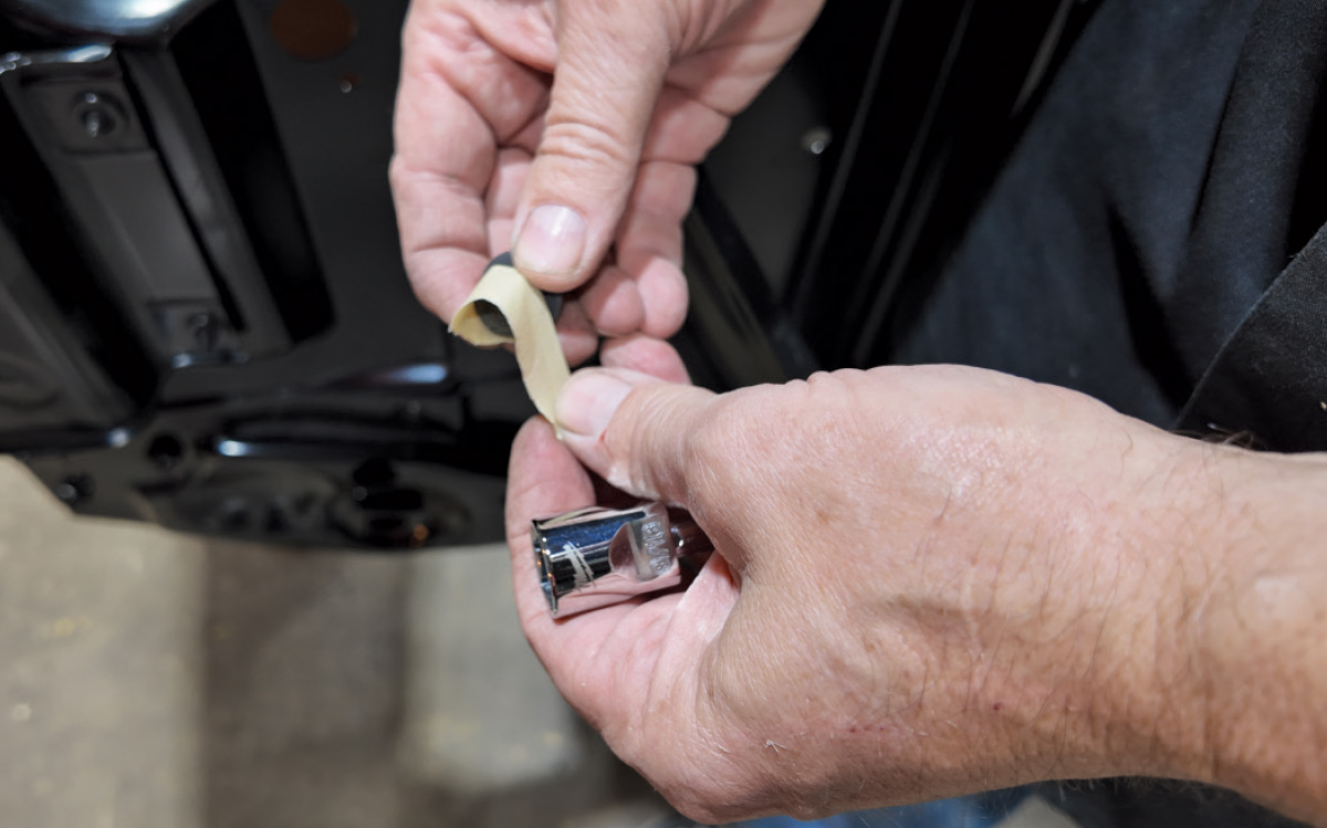 Close-up of hands applying masking tape to a small black component near a silver metal socket.