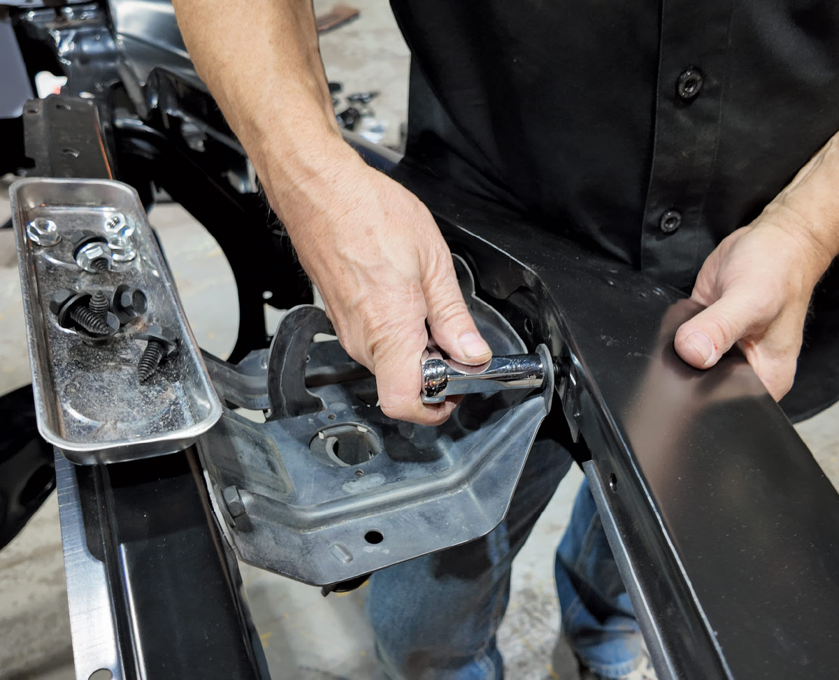 Close-up of hands using a socket wrench to bolt a metal bracket onto a black car frame.