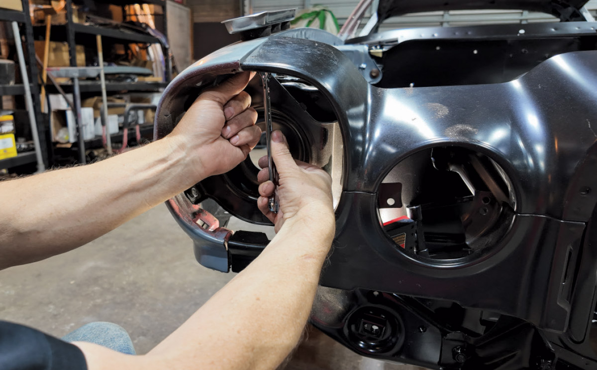 Hands using a wrench to secure a black headlight housing piece into a car body.