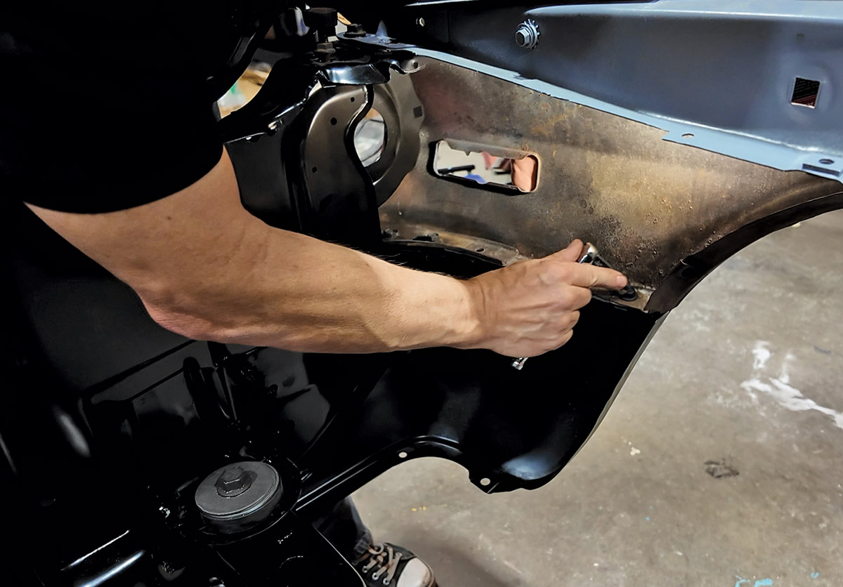 A mechanic's arm uses a wrench to tighten a bolt inside a car's wheel well.