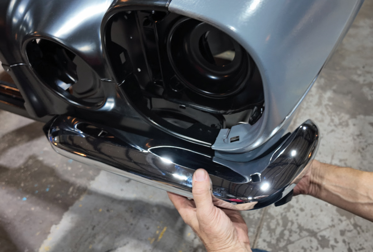 Hands carefully install a chrome bumper onto a blue primed car fender.