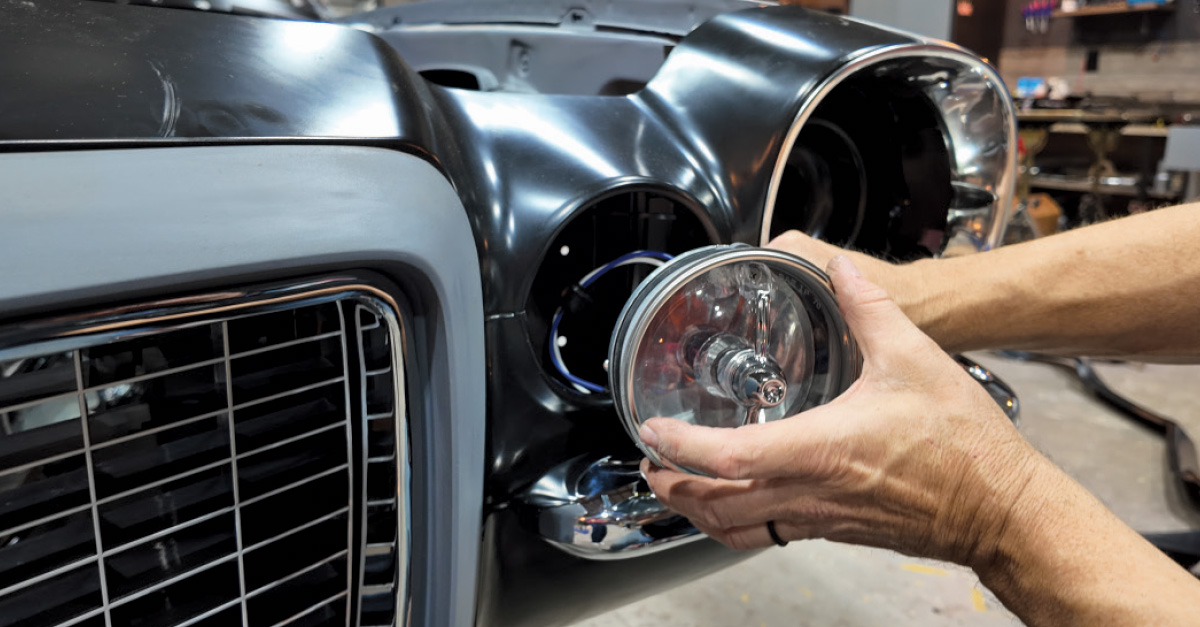 A mechanic installs a round parking light lens into a black headlight housing on a car.