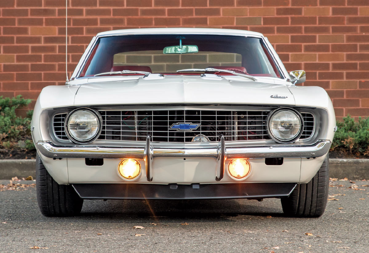 Direct front view of the white Camaro with illuminated amber fog lights and a blue Chevrolet bowtie emblem on the grille.