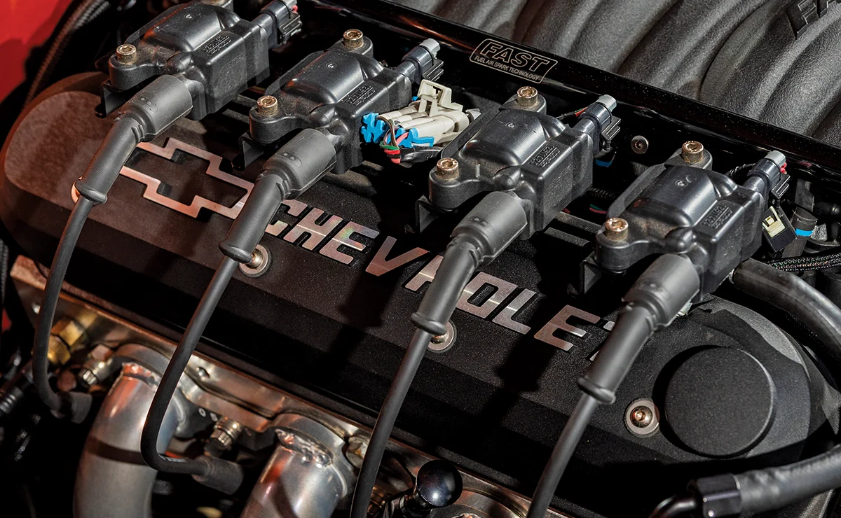 A detailed view of a high-performance car engine bay showcasing the ignition coil packs and spark plug wires mounted on top of a sleek, black textured valve cover with embossed silver Chevrolet branding