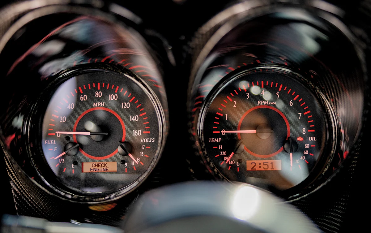 A detailed shot of high-performance car instrument clusters with red accent lighting. The left gauge shows speed and fuel levels, while the right gauge monitors RPM, engine temperature, and oil pressure