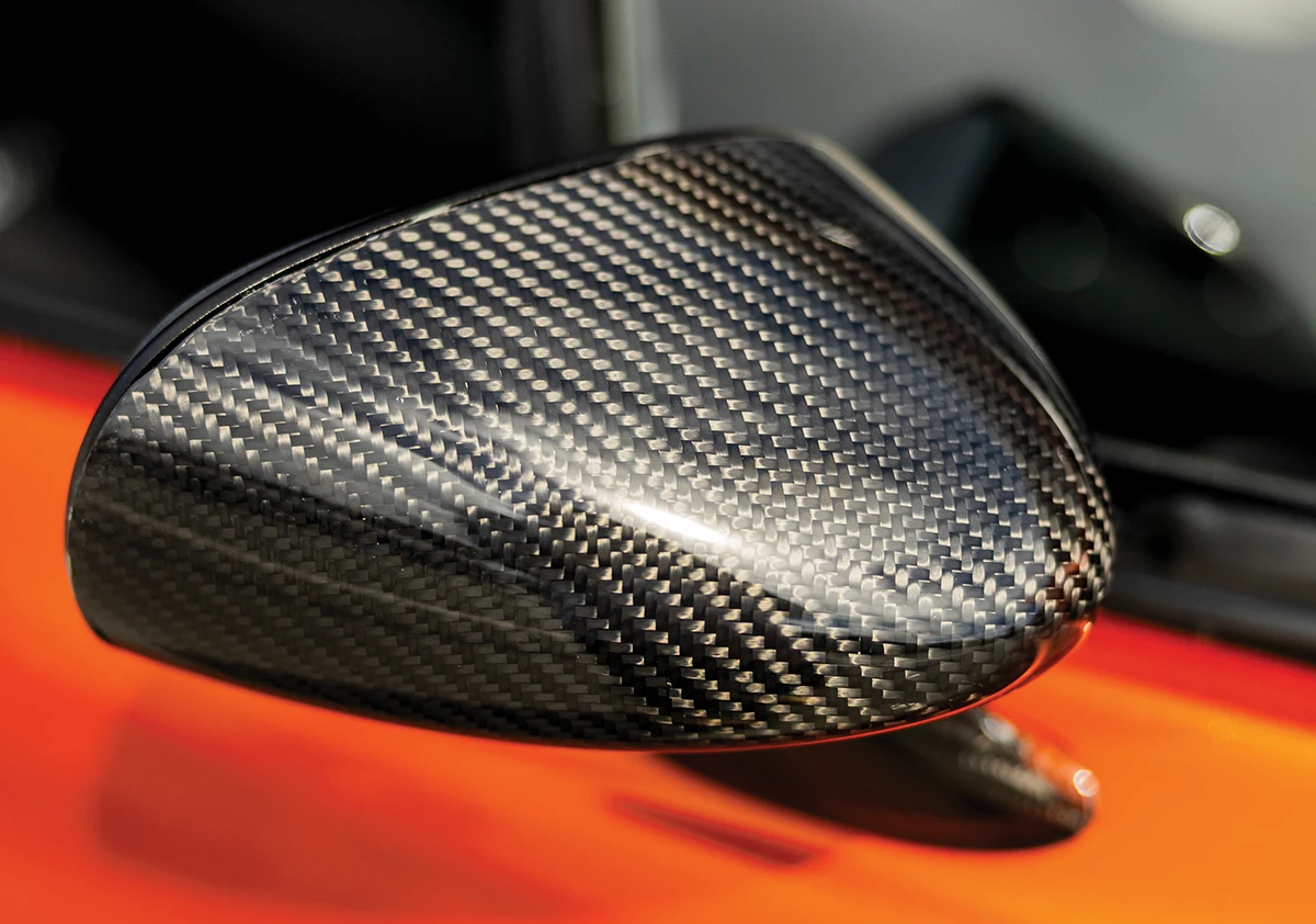 Close-up detail of a custom carbon fiber side mirror on a metallic orange 1968 Chevrolet Camaro, showcasing the high-gloss weave pattern and aerodynamic pro-touring design