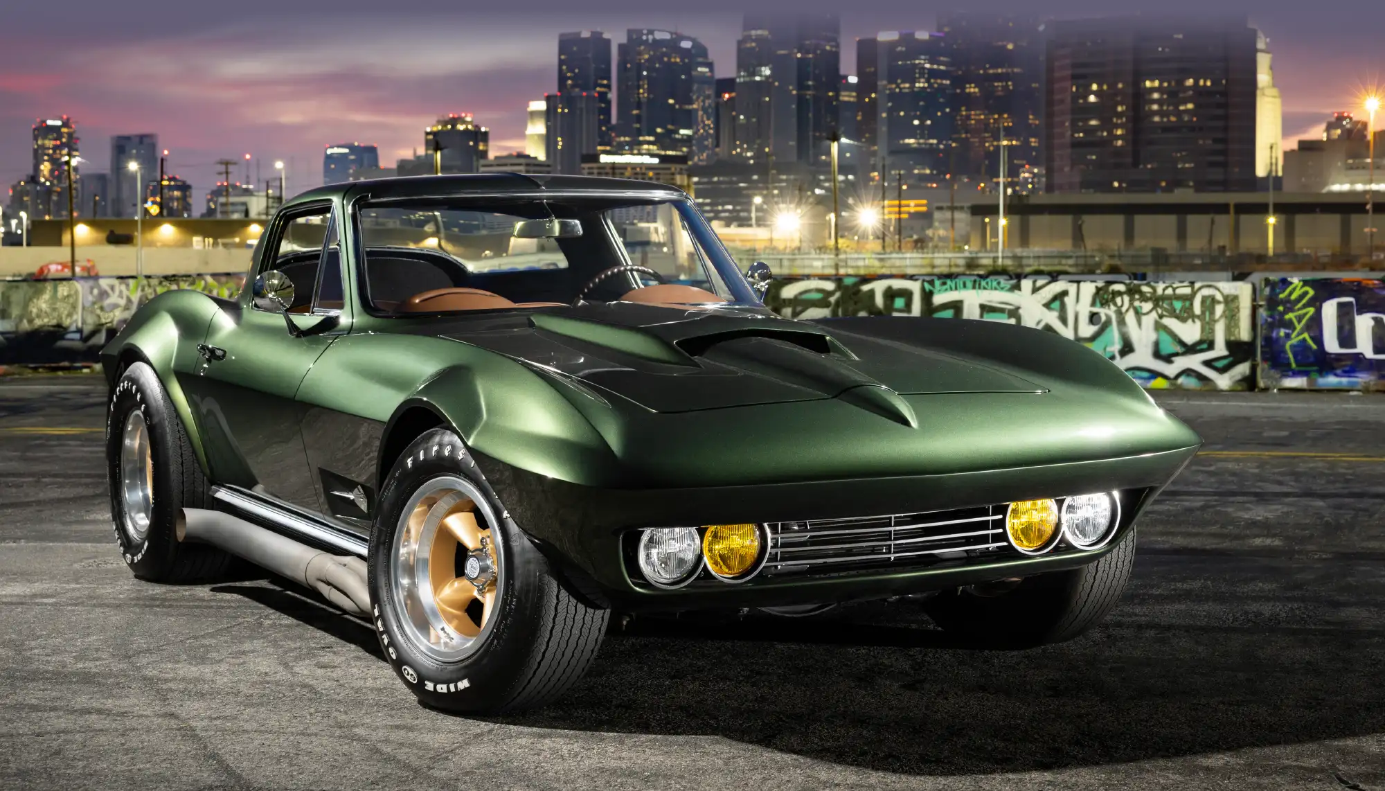 A classic dark green Chevrolet Corvette with side exhaust pipes and gold wheels at dusk.