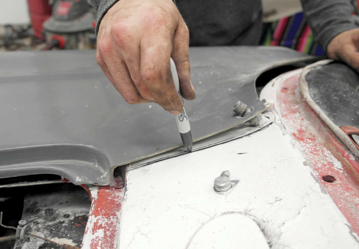 A close-up of a person using a black Sharpie marker to trace a line along the edge of a grey car body panel