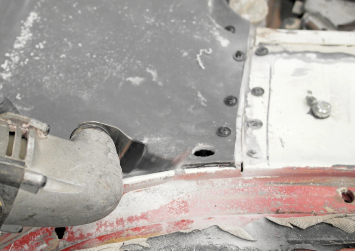 An oscillating multi-tool is used to trim the edge of a grey fiberglass panel installed on the vehicle's metal frame
