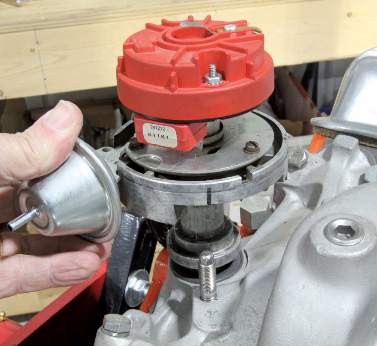 A hand positioning the distributor housing into the intake manifold to ensure proper gear engagement.