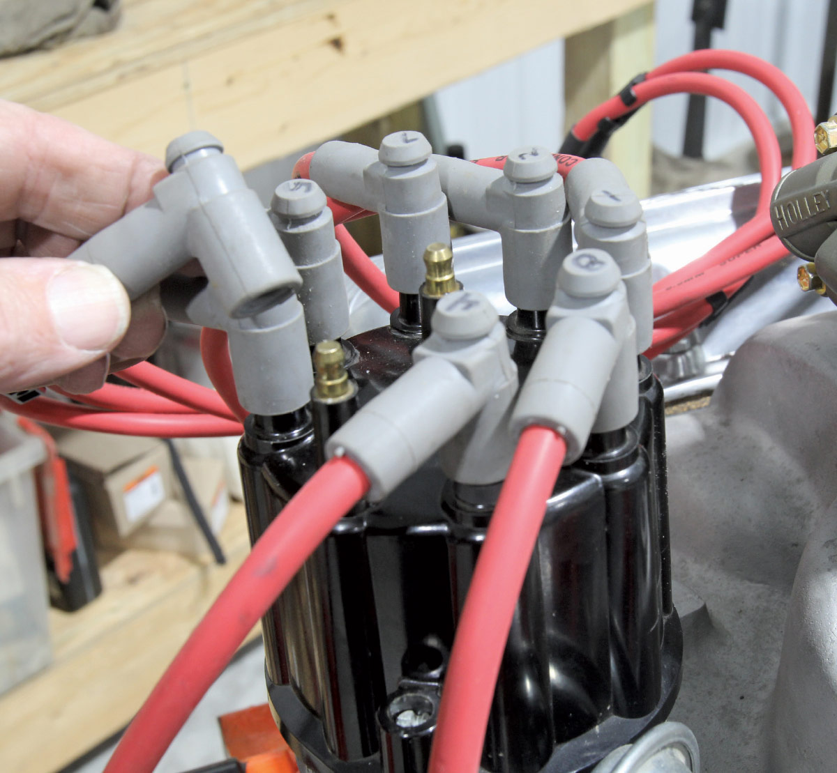 Hand connecting red spark plug wires to a black distributor cap on a V8 engine.