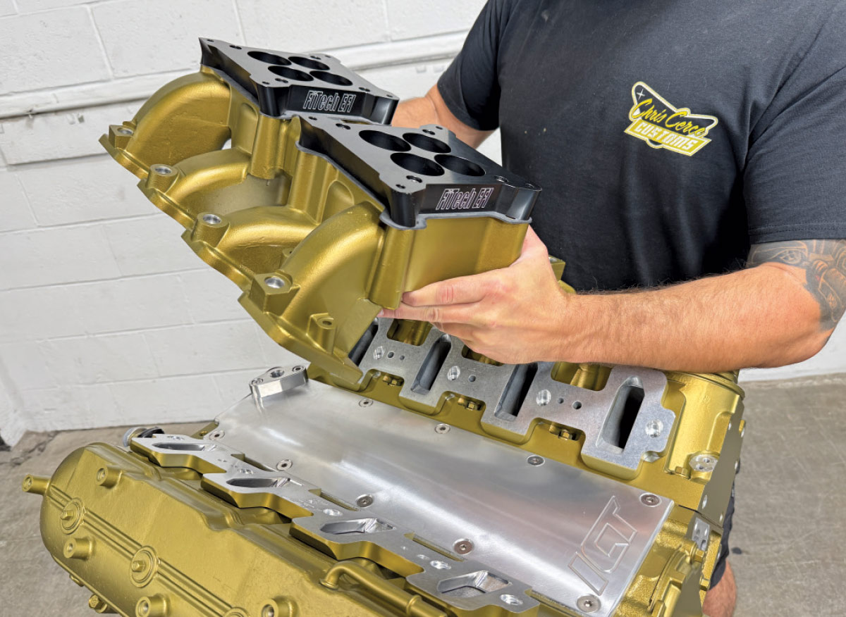 Mechanic lowering a gold intake manifold with black FiTech spacers onto the gold engine block.