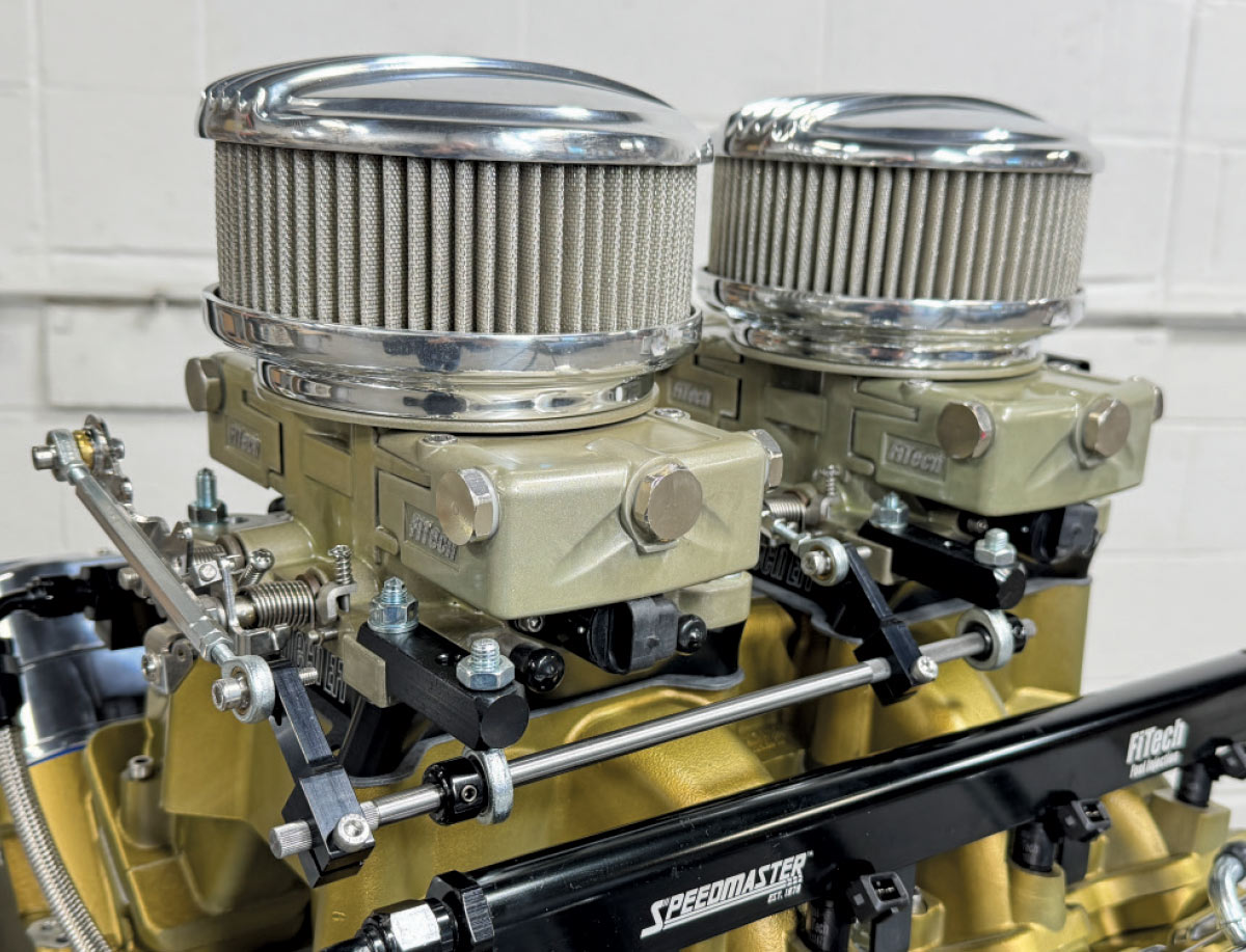 Close-up of dual FiTech fuel injection throttle bodies with chrome air cleaners and a central linkage rod.