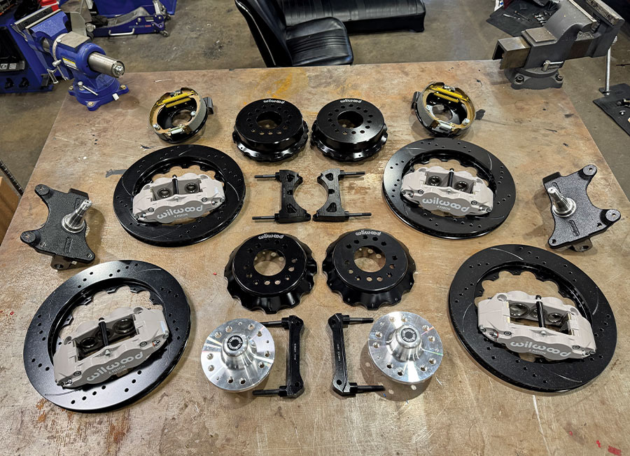 A complete set of new Wilwood high-performance big brake kit components, including gray 6-piston calipers, black slotted and drilled rotors, hubs, spindles, and mounting hardware, neatly arranged on a workbench