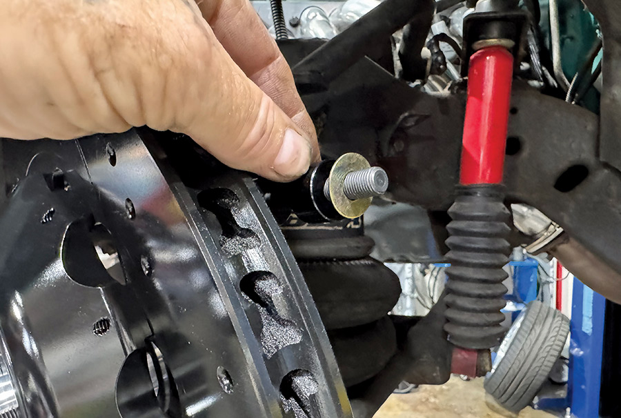 A hand positions a mounting bolt and gold washer behind a black vented brake rotor