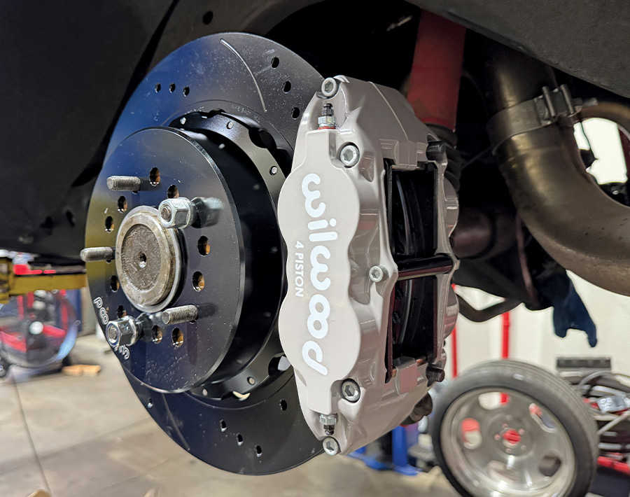 Close-up of a newly installed Wilwood 4-piston brake caliper and a black slotted and drilled rotor on a vehicle suspension
