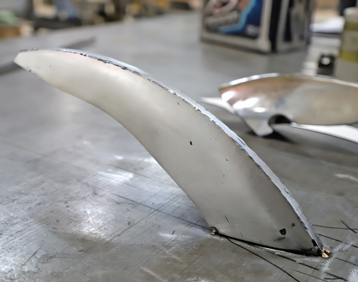 Metal bumper strake standing upright on a workbench, tack-welded at the base to hold the halves together during assembly.