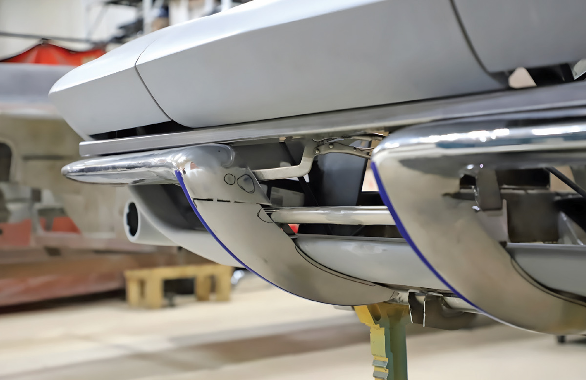 Front bumper of a grey C2 Corvette during a test fit. A metal strake is held against the bumper with locking pliers, featuring blue tape and marker notations for adjustment.