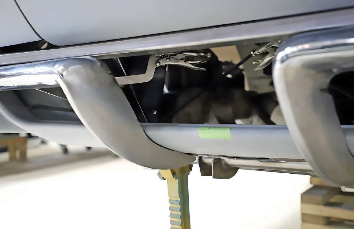 Lower front bumper assembly of a C2 Corvette with metal strakes and chrome components held in place by locking pliers during fabrication.