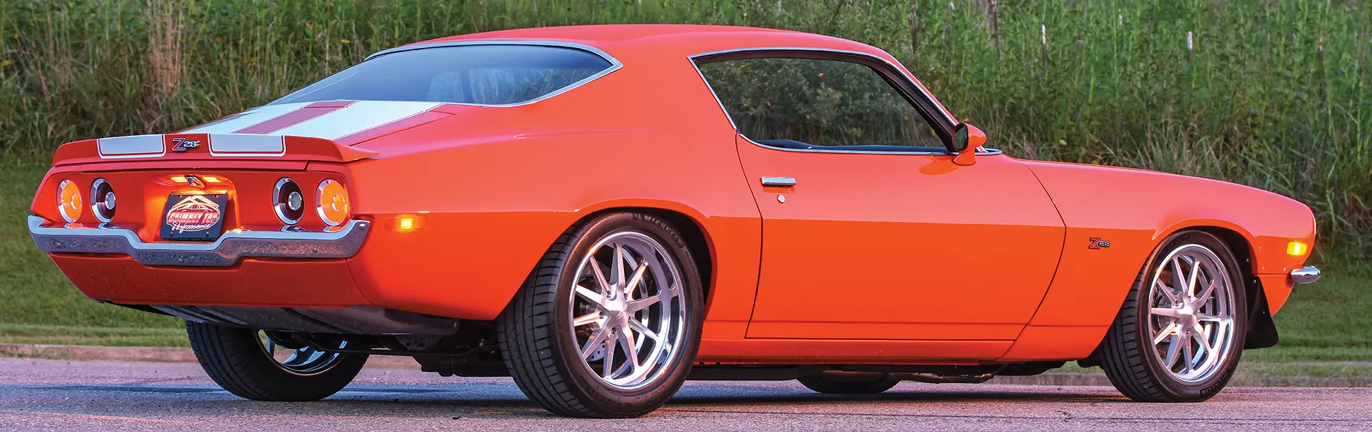 Rear three-quarter view of orange Camaro with white Z28 stripes.