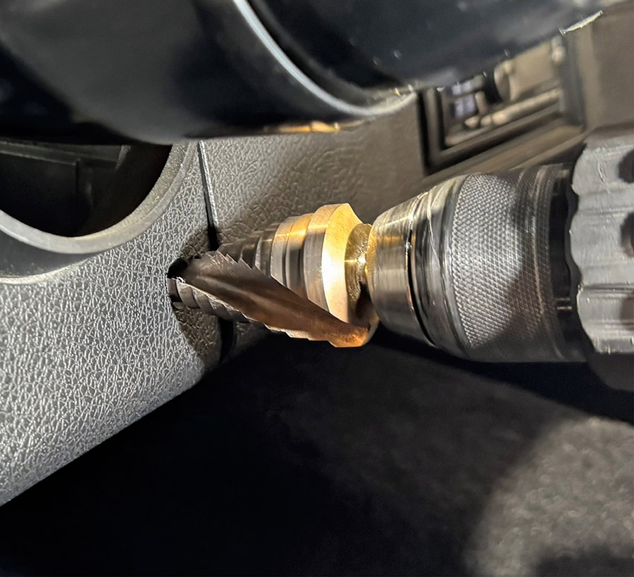 A step drill bit is used to bore a hole into a vehicle dashboard panel.