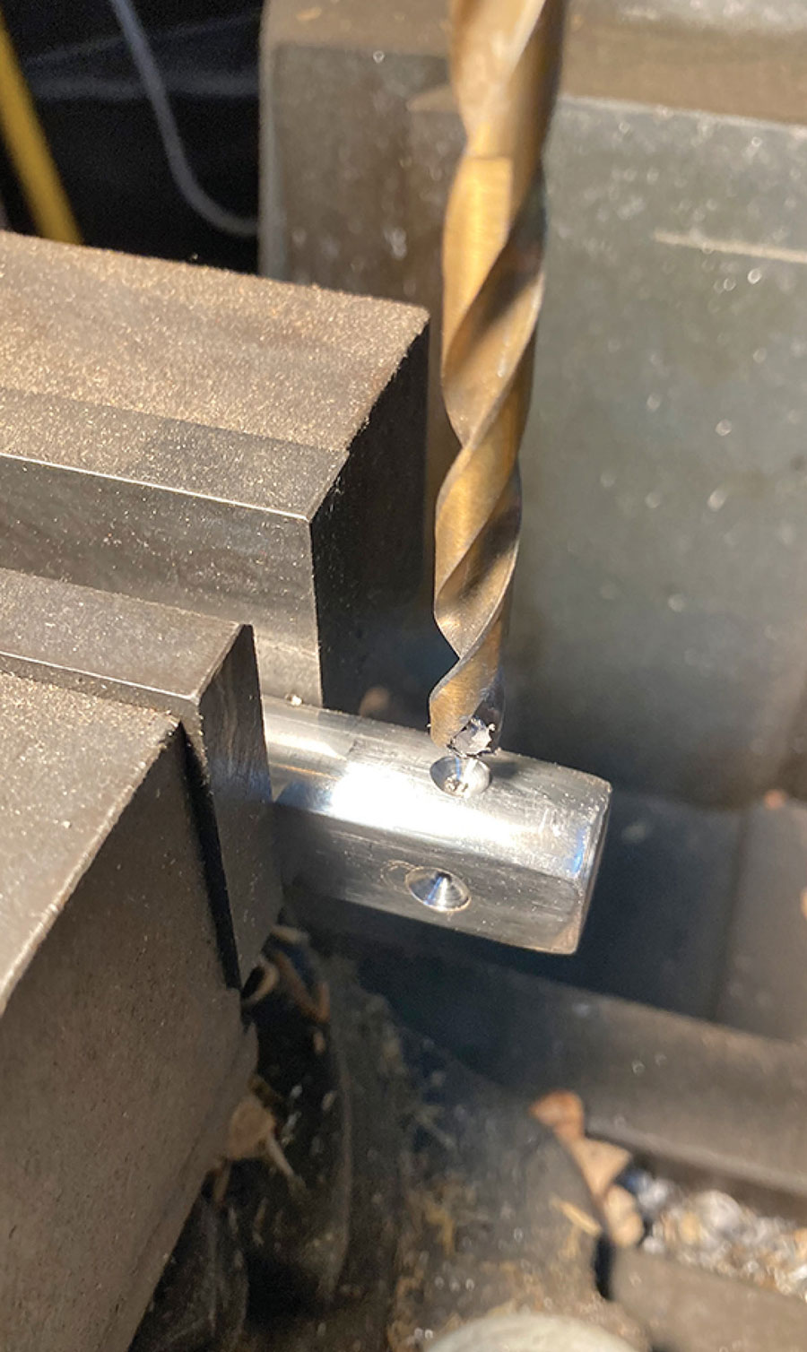 Drill bit creating a dimple in a metal shaft held in a vise.