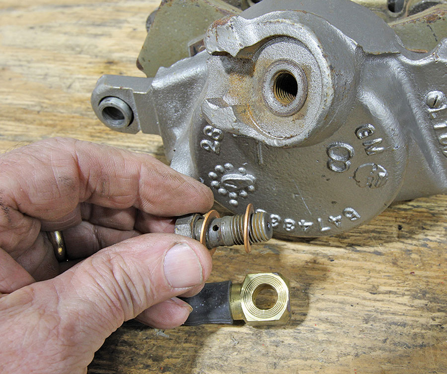 Hand holding a banjo brake fitting with copper washers and a mounting bolt.
