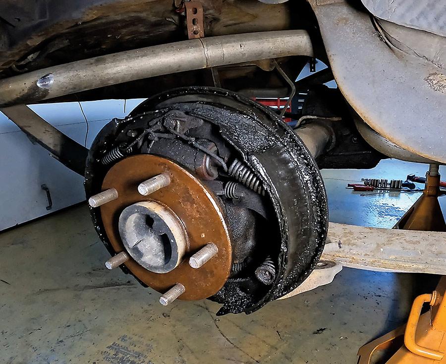 Dirty and oil-soaked rear drum brake assembly requiring a complete rebuild.