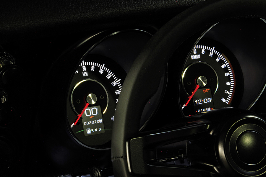 An illuminated car dashboard displaying a digital speedometer, tachometer, clock, and steering wheel.
